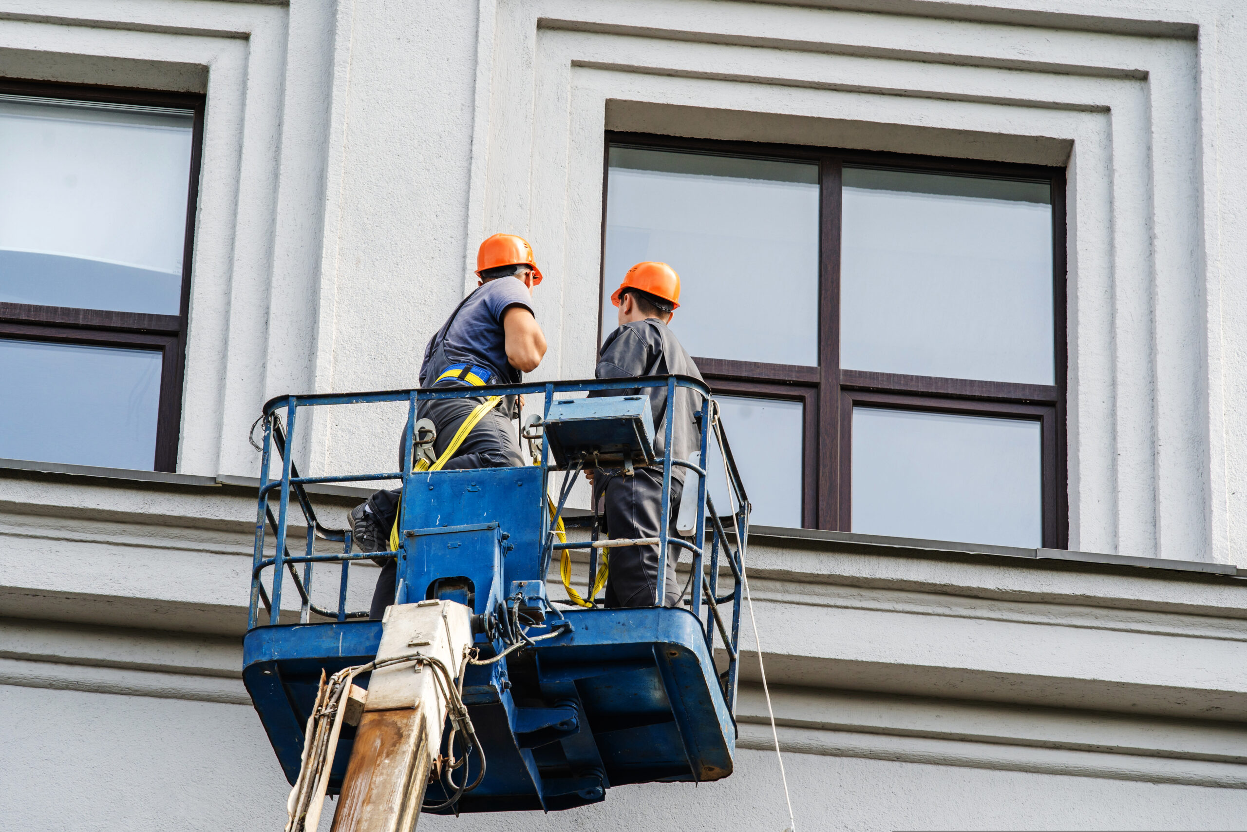 Workers are restoring the facade of the building while standing on a special platform. Home wall repair with the help of a lifting tower. Unrecognizable people
