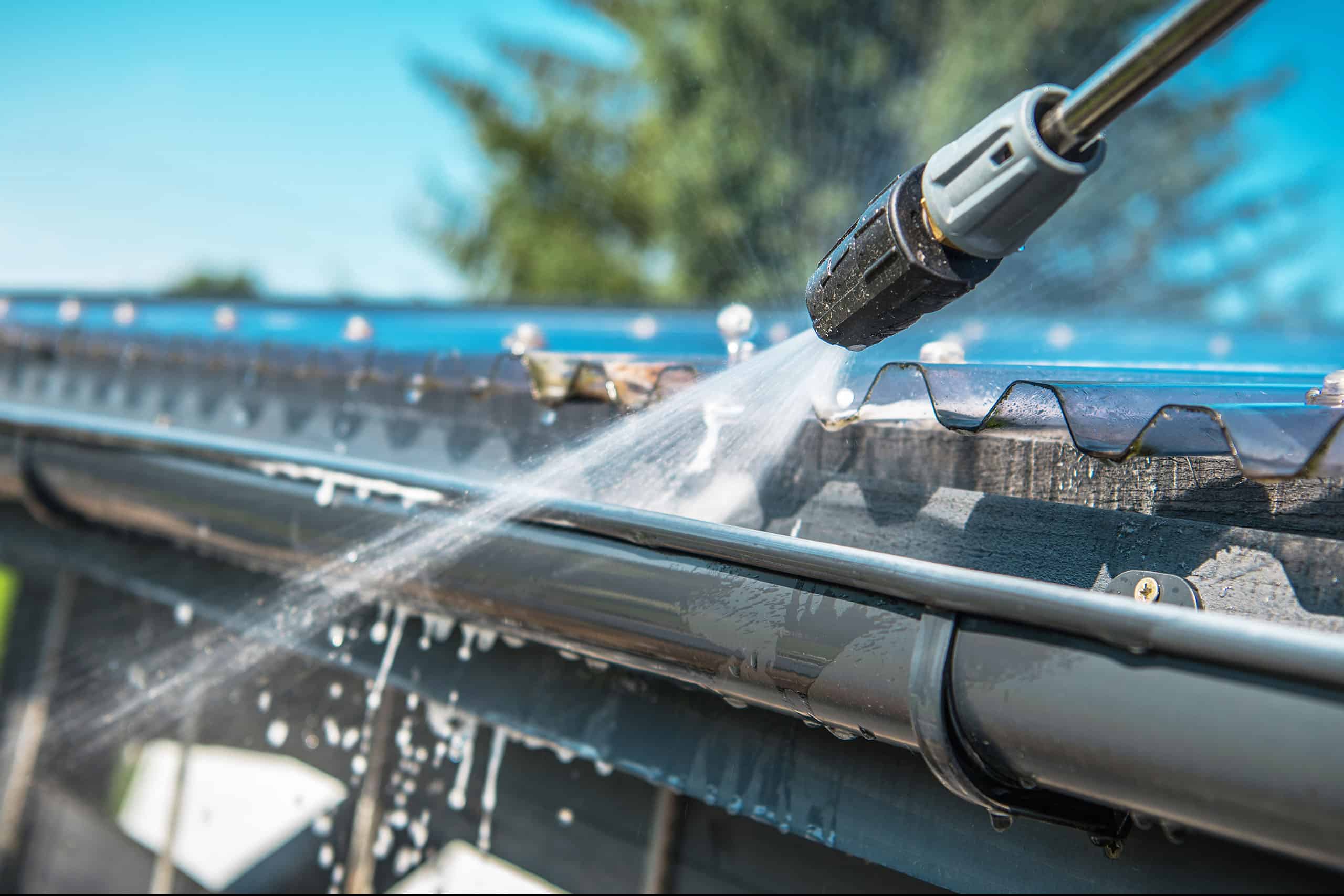 Pressure washer spraying water to clean gutters.